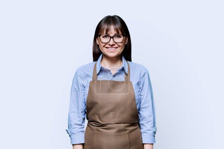Confident smiling middle-aged woman in apron on white background. Successful mature female small business owner service worker entrepreneur looking at camera. Business work people startup advertising