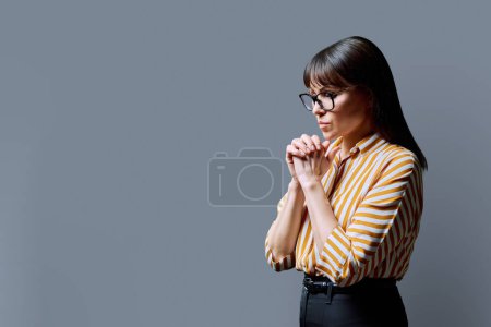Photo for Upset sad serious mature woman in glasses with folded hands, copy space grey background. Loneliness problems illness difficulties, depression, prayer, mental health, middle age concept - Royalty Free Image