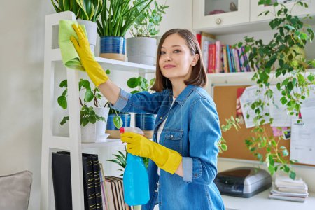 Foto de Mujer joven haciendo limpieza de la casa, limpiando el polvo, usando guantes con detergente limpiador spray trapo en el interior de la habitación. Limpieza casera rutinaria, limpieza tareas domésticas estilo de vida doméstico - Imagen libre de derechos