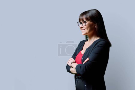 Téléchargez les photos : Portrait de profil d'une femme souriante mature et confiante sur fond de studio gris. Femme heureuse d'âge moyen regardant de côté, copier l'espace pour l'image de texte publicitaire. Services aux entreprises éducation santé - en image libre de droit