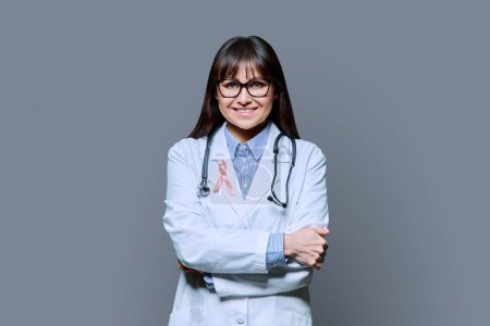Foto de Retrato de doctora sonriente en bata de laboratorio blanca con cinta rosa que simboliza el Día Internacional del Cáncer de Mama sobre fondo gris. Tratamiento diagnóstico de cáncer de mama, medicina, salud de la mujer - Imagen libre de derechos