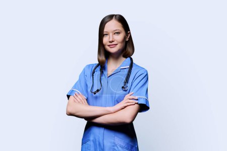 Téléchargez les photos : Portrait de jeune infirmière souriante confiante avec stéthoscope, bras croisés, regardant la caméra sur fond de studio blanc. Services médicaux, santé, assistance professionnelle, concept de soins médicaux - en image libre de droit