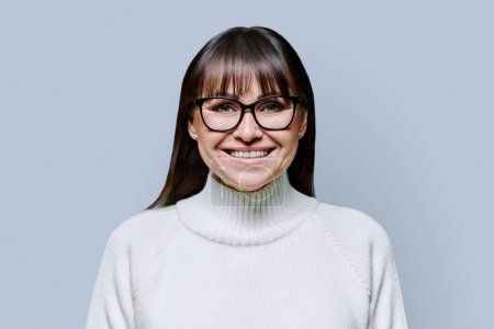Photo for Headshot portrait middle-aged beautiful smiling woman in white sweater on gray studio background. Happy confident mature female in glasses looking at camera. Beauty lifestyle business work, 40s people - Royalty Free Image