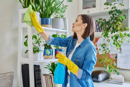 Foto de Mujer joven haciendo limpieza de la casa, limpiando el polvo, usando guantes con detergente limpiador spray trapo en el interior de la habitación. Limpieza casera rutinaria, limpieza tareas domésticas estilo de vida doméstico - Imagen libre de derechos