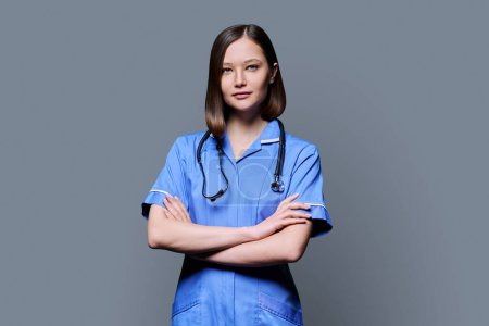 Photo for Portrait of young confident smiling female nurse with stethoscope, crossed arms, looking at camera on gray studio background. Medical services, health, professional assistance, medical care concept - Royalty Free Image