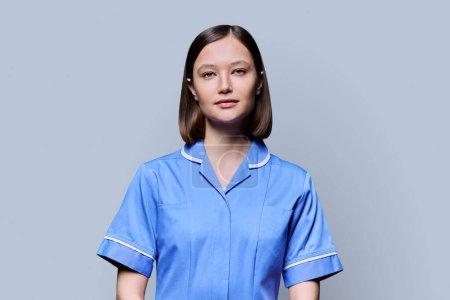 Foto de Retrato de una joven enfermera sonriente confiada mirando a la cámara en un fondo gris de estudio. Servicios médicos, salud, asistencia profesional, concepto de atención médica - Imagen libre de derechos
