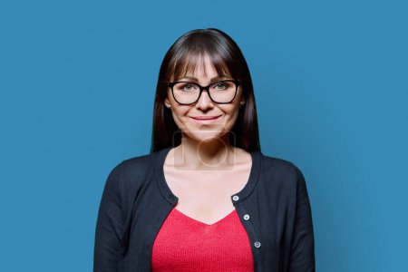 Photo for Portrait of confident smiling happy middle aged woman on blue background. Positive female with glasses looking at camera. 40s professional, beauty health lifestyle work business services - Royalty Free Image