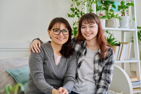 Photo for Portrait of happy hugging mother and teenage daughter sitting together on couch, smiling looking at camera. Two generations of family, communication, motherhood, friendship, relationship, mothers Day - Royalty Free Image