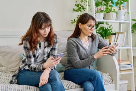 Photo for Mother and teenage daughter sitting on the couch at home, using smartphones. Technology, lifestyle, two generations of family, motherhood, relationship concept - Royalty Free Image