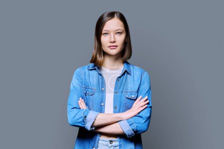 Photo for Young beautiful confident woman with crossed arms on gray studio background. Serious attractive 20s female in denim looking at camera. Lifestyle, fashion beauty style, youth business work education - Royalty Free Image