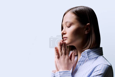 Photo for Close-up profile view of young woman with folded hands on white background, copy space. Serious female with closed eyes worried praying thinking. Mental health psychology psychotherapy feelings stress - Royalty Free Image