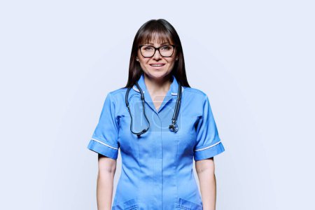 Portrait of smiling middle-aged woman nurse in blue with stethoscope on white studio background. Medical services, nhs, health, professional assistance, medical care concept