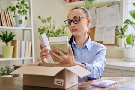 Photo for Satisfied female consumer buyer sitting at home unpacking cardboard box with online purchases. Woman unpacking boxes with cosmetics care products perfumes. Delivery by mail, internet online store - Royalty Free Image