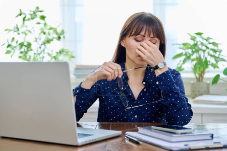 Tired sad mature woman at workplace at table with computer laptop, holding hands on head. Middle age people, stress difficulty, headache health, lifestyle concept