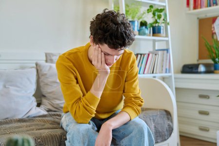 Photo for Sad upset tired young man sitting on couch at home, touching his head with hands. Health problems, headaches, troubles, difficulties in study, family relationships, mental health, stress, depression - Royalty Free Image