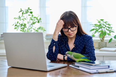 Mujer madura triste cansada en el lugar de trabajo en la mesa con ordenador portátil, cogido de la mano en la cabeza. Personas de mediana edad, dificultad para el estrés, dolor de cabeza salud, concepto de estilo de vida