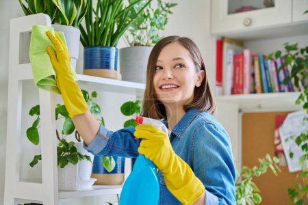 Photo for Young woman doing house cleaning, wiping dust, wearing gloves with cleaning detergent agent spray rag in room interior. Routine home cleaning, cleanliness housework housekeeping household lifestyle - Royalty Free Image