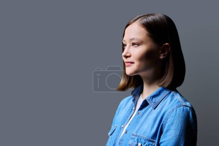 Téléchargez les photos : Portrait de profil de jeune femme souriante sur fond de studio gris. 20s heureux féminin regardant vers le côté, copier l'espace pour l'image de texte publicitaire. Services aux entreprises, éducation, santé beauté - en image libre de droit