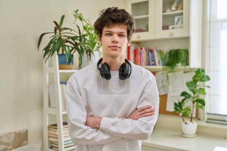 Photo for Portrait of young handsome guy with crossed arms, in home interior. Smiling confident male 19-20 years old with curly hairstyle looking at camera. Lifestyle, youth concept - Royalty Free Image