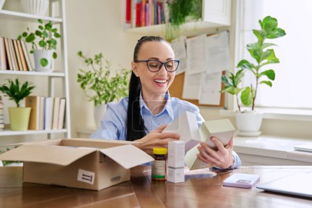 Photo for Satisfied female customer buyer sitting at home unpacking cardboard box with online purchases. Happy woman unpacking boxes with cosmetics care products vitamins perfumes. Delivery by mail online store - Royalty Free Image