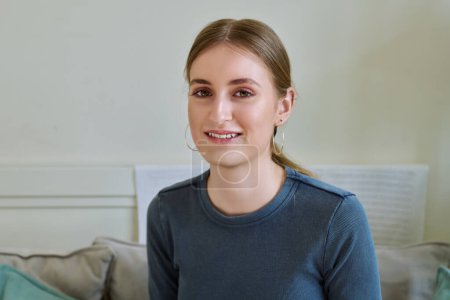 Téléchargez les photos : Portrait d'une belle adolescente souriante et heureuse regardant la caméra, assise sur le canapé à la maison. Age 16,17,18 ans, style de vie, concept jeunesse - en image libre de droit