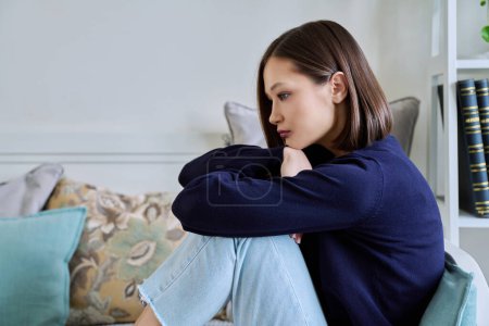 Photo for Young sad upset unhappy woman sitting on couch at home. Frustrated confused female experiencing difficulties. Mental problems, feelings, loneliness, stress, depression, difficulties, youth concept - Royalty Free Image