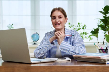 Foto de Retrato de la escuela secundaria, estudiante universitaria sonriendo joven sentada en el escritorio con computadora portátil mirando a la cámara. Educación, formación, e-learning, 16,17,18 años - Imagen libre de derechos