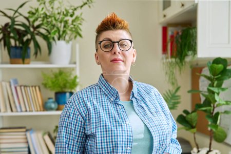 Photo for Portrait of smiling middle-aged woman in glasses with red haircut looking at camera in home interior. Mature people, lifestyle, health, life concept - Royalty Free Image