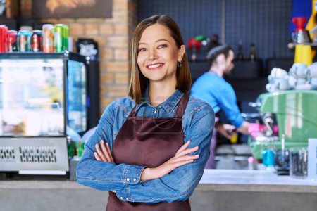 Photo for Confident successful young woman service worker in apron with crossed arms looking at camera in restaurant cafeteria coffee pastry shop. Small business, staff, occupation, entrepreneur owner, work - Royalty Free Image