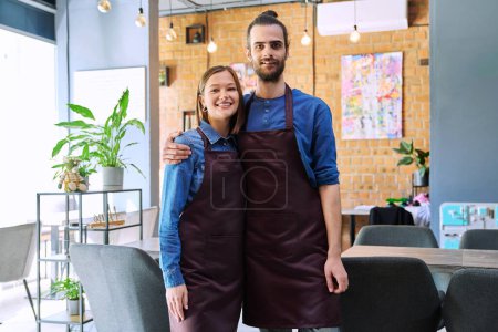 Photo for Small business team portrait of hugging of successful colleagues partners young man woman in aprons posing looking at camera at workplace in restaurant coffee shop cafeteria. Partnership teamwork work - Royalty Free Image