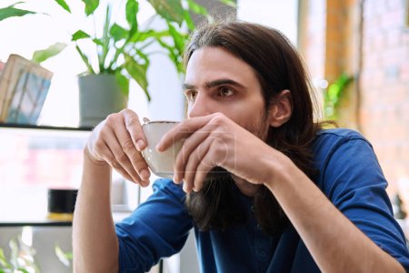 Foto de Primer plano de un joven guapo sosteniendo la taza de café mientras está sentado en el restaurante de la cafetería. Estilo de vida, ocio, relajación, bebidas de café, concepto de personas - Imagen libre de derechos