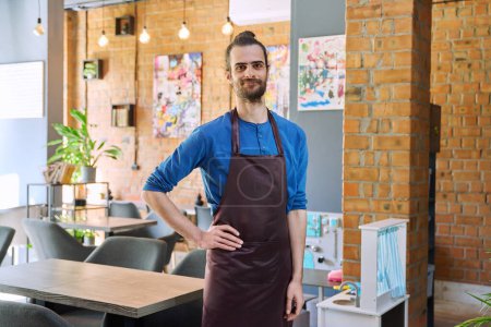 Photo for Confident successful young man service worker owner in apron, handsome male looking at camera in restaurant cafeteria coffee pastry shop interior. Small business staff occupation entrepreneur work - Royalty Free Image