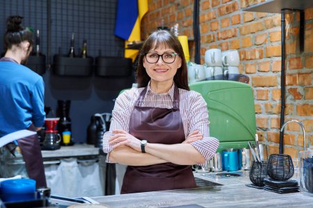 Photo for Portrait of 40s female small business owner entrepreneur in apron with crossed arms standing behind bar counter in coffee shop cafeteria cafe. Staff teamwork work service retail management success - Royalty Free Image