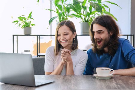 Happy smiling surprised young couple looking at laptop together while sitting in cafe, cafeteria. Leisure time for two, lifestyle, togetherness, relationship, communication, work study remotely