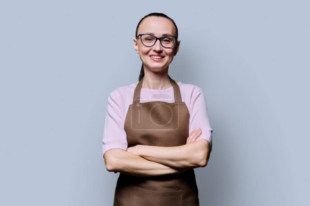 Photo for Portrait of confident smiling 30s woman in apron on grey background. Successful female small business owner, service worker looking at camera with crossed arms. Staff, management, advertising, people - Royalty Free Image