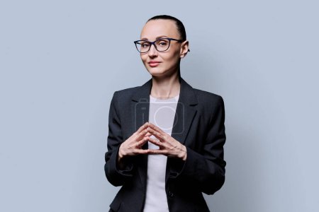Photo for Portrait of thinking serious 30s business woman on grey studio background. Confident female in glasses, suit looking at camera. Business work teaching job career people concept - Royalty Free Image