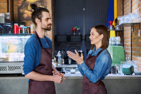 Photo for Small business team, successful colleagues partners workers young man and woman in aprons talking at workplace in restaurant coffee shop cafeteria. Cooperation, partnership, teamwork, staff, work - Royalty Free Image