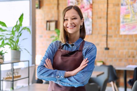 Photo for Confident successful young woman service worker owner in apron with crossed arms looking at camera in restaurant cafeteria coffee pastry shop interior. Small business staff occupation entrepreneur - Royalty Free Image