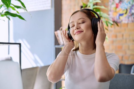 Photo for Young happy woman in headphones with closed eyes enjoying music, audio text book. Technology, lifestyle, youth concept - Royalty Free Image