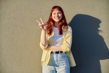 Young smiling beautiful attractive red-haired hipster female with facial piercing looking at camera outdoor, gray solar wall background. Beauty, fashion, piercing, style, lifestyle youth concept