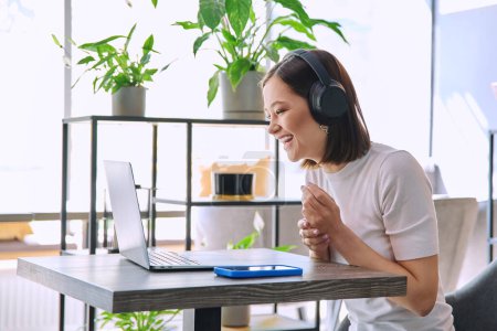 Photo for Young woman in headphones having video chat conference call using laptop computer sitting in coworking cafe. Female college student studying online listening webinar preparing exam, working remotely - Royalty Free Image