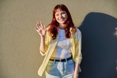 Outdoor portrait of happy beautiful young hipster female with red hair facial piercing looking at camera against sunny gray wall background. Beauty, youth, fashion, joy, happiness, lifestyle concept