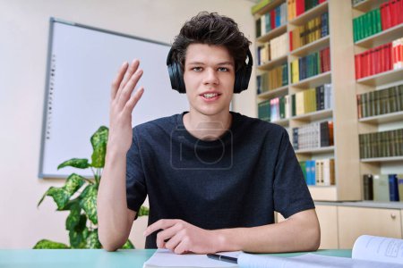 Web-Cam-Porträt von College-Student Kerl mit Kopfhörern suchen im Gespräch mit der Kamera in Bildungsgebäude Bibliothek Klassenzimmer. Videotelefonkonferenz, Online-Unterrichtsprüfung, technische Ausbildung