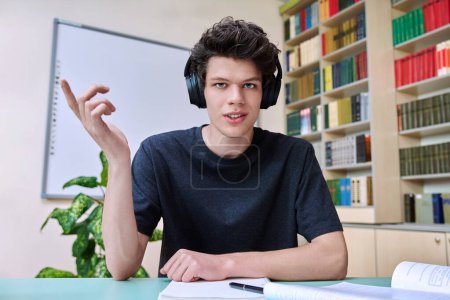 Web-Cam-Porträt von College-Student Kerl mit Kopfhörern suchen im Gespräch mit der Kamera in Bildungsgebäude Bibliothek Klassenzimmer. Videotelefonkonferenz, Online-Unterrichtsprüfung, technische Ausbildung