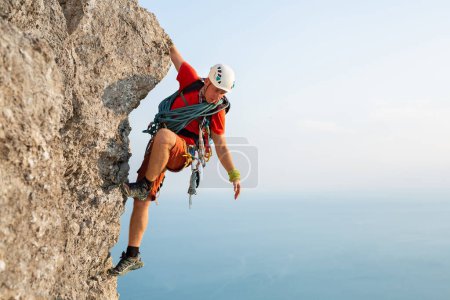 Young male climber climbs a difficult route with a view of the sea at sunset