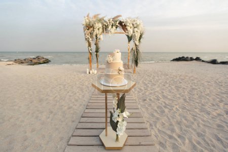 Pastel de boda en una boda en la playa en el fondo de un hermoso arco para una ceremonia de salida