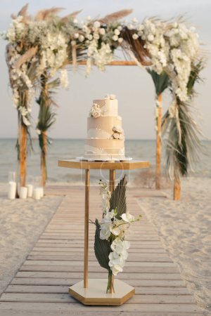 Téléchargez les photos : Gâteau de mariage lors d'un mariage à la plage sur le fond d'une belle arche pour une cérémonie de sortie - en image libre de droit