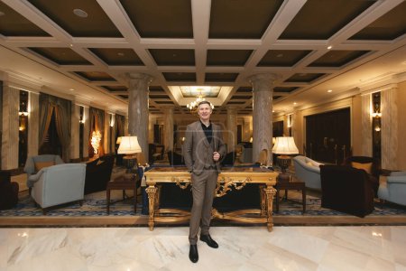 Foto de Hombre de negocios en un clásico se encuentra en el lujoso interior del hotel y muestra un pulgar hacia arriba - Imagen libre de derechos