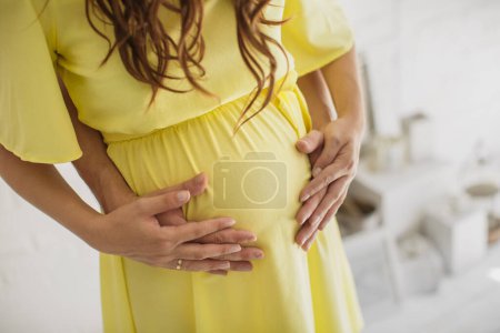 Téléchargez les photos : Cropped image de belle femme enceinte et son beau mari étreignant le ventre - en image libre de droit