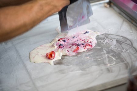 Gebratene Eisbrötchen in der Tiefkühlpfanne umrühren. Rolleis, handgemachtes Eis-Dessert. Gebratene Eismaschine mit Stahl-Kühlpfanne.